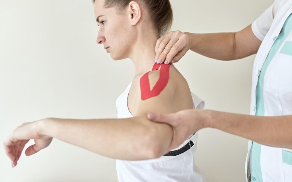 Physiotherapist performing brachial plexus injury exercises with a patient using kinesiology tape on the shoulder to aid recovery.
