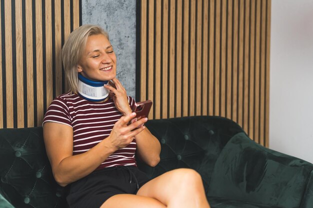 Young woman wearing a cervical collar and using her phone while recovering from neck pain, learning about neck fusion recovery time and exercises for rehabilitation.
